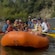 Group of smiling Guests in life jackets raft on a river near a sandy shore and forested hills